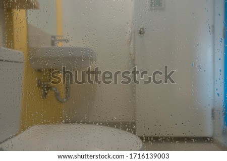 Water droplets on glass in bathroom walls as the background and has washbasin and toilet is are used for design work.