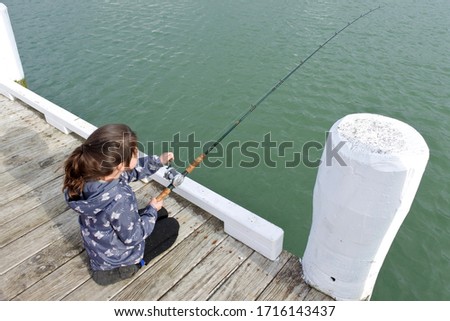 Young girl (age 10) holding a fishing rod fishing from a boat jetty. Real people. Copy space