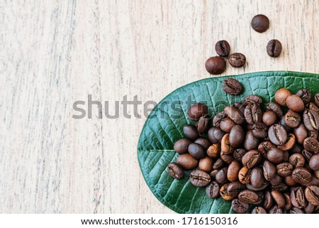 Coffee beans on a green leaf and scattered on a light wooden table, fragrant fried beans for freshly americano, espresso, natural background, top view, closeup grains, flat lay, copy space