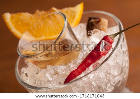 tequila in a glass on a pillow of crushed ice in a bowl, served with chili, orange and caramelized sugar. close-up. macro