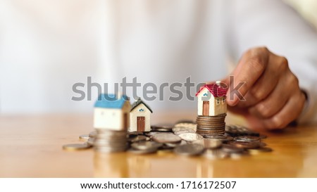 Closeup image of a woman's hand putting house model on pile of coins for saving money concept Royalty-Free Stock Photo #1716172507