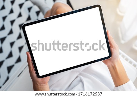 Top view mockup image of a woman holding black tablet pc with blank white desktop screen while sitting in bedroom with feeling relaxed in the morning Royalty-Free Stock Photo #1716172537