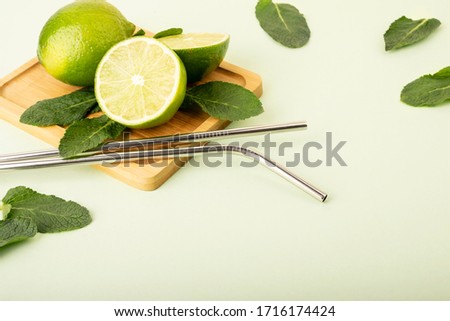Reusable metal straws on a pastel background. Fresh lime and mint fruits lie on a wooden stand. Green color and fruts emphasize. Reusable environmental products, zero waste.Eco products Royalty-Free Stock Photo #1716174424