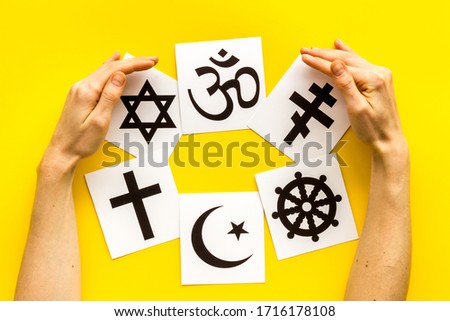 World religions concept. Hands hugs Christianity, Catholicism, Buddhism, Judaism, Islam symbols on yellow background top view