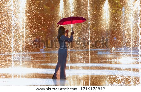 Young girl in white dress holding red umbrella and walking on the fountain - Picturesque Park Paillon Promenade - Nice, France