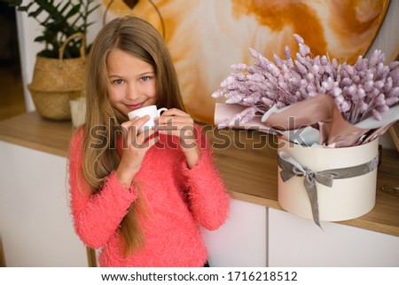 cute little girl in coral sweater, with white cup in her hands, in room with  home interior