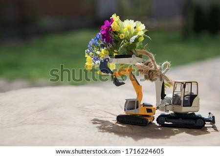 bouquet on the arrow of an excavator. 2 toy excavator models on a bright sunny day. Concept of love, business - congratulation, builder's day holiday
greeting card for the construction business