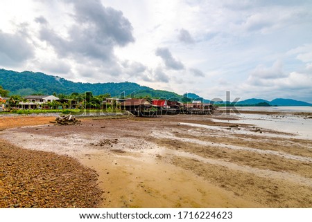 View of fishermen village at Ko Lanta island, Thailand. Old wooden houses are build above sea. Jungle and forest on hills in background. Cloudy weather before storm.