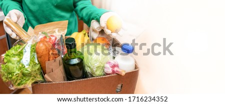 Woman in protective gloves taking food products out of delivered box in kitchen. Safe delivery. Contactless home delivery. Food donation. Stock for rainy day. Selective focus. Banner, copy space.