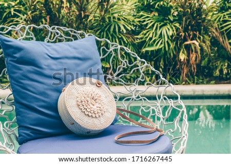 Trendy round crossbody straw bag with seashells on the beautiful lounge chair near a pool. Summer outfit, vacation, holiday concept. Travel background with place for text