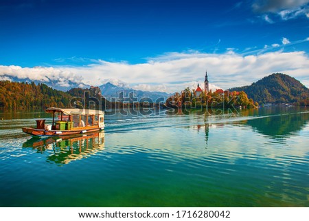 Church of Assumption in Lake Bled, Slovenia with blue sky, touristic boat and clouds in the autumn