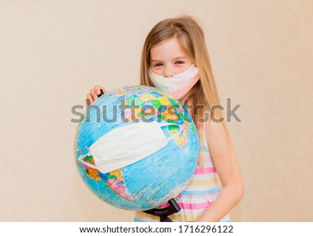 little girl in a medical mask holds a globe in her hands, wrapped in a medical mask. Little girl heals the planet. The concept of air and environmental pollution by human activities.