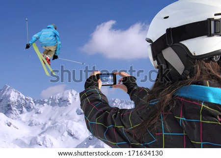 A young girl by mobile phone photographs of skiers jump
