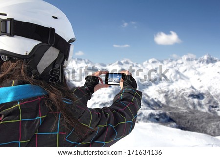Girl taking pictures on a mobile phone winter landscape, mountains under snow