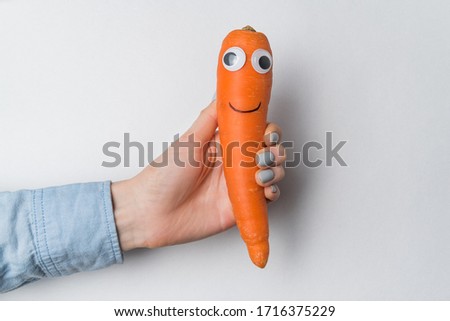 Hand holding carrot with a funny face on white background. Carrot character with eyes and smile.