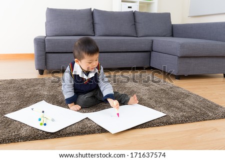 Little boy drawing picture and seating on carpet