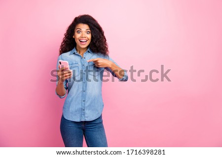 Look black firday. Addicted surprised afro american girl use smartphone point index finger impressed social network news wear denim jeans shirt isolated over pink color background
