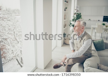 Photo of white haired aged man looking window deep thinking leaning sofa indoors