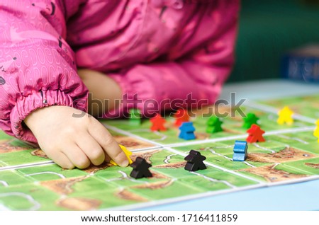 Board game and kids leisure concept - little girl hold yellow people figure in hand. red, black, blue, green wood chips in children play