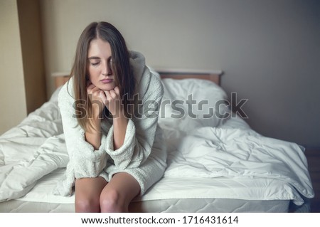 a young woman sits on the edge of the bed closing her eyes and propping her head in her hands. fatigue, depression, insomnia, quarantine, isolation Royalty-Free Stock Photo #1716431614