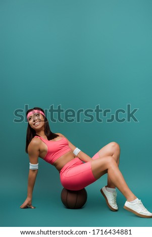 Happy african american sportswoman sitting on ball and smiling on green background