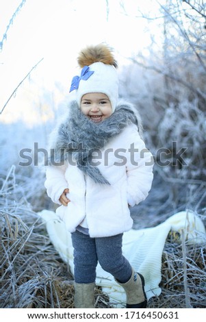 little happy girl in white jacket and white hat with blue bow-knot
 in winter fairy tail  runs on the valley