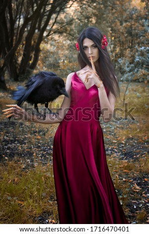Art photo of a fairy forest nymph in the autumn forest with a big black raven on his hand