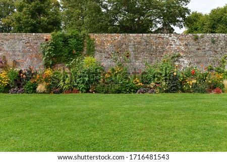 A Scenic View of a Beautiful English Style Landscape Garden with a Green Mowed Lawn, Colourful Flower Bed and  Weathered Redbrick Wall Royalty-Free Stock Photo #1716481543