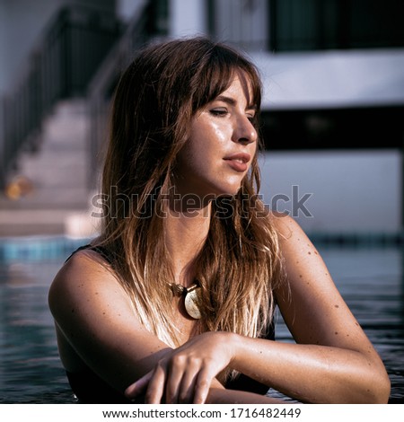 
A brunette in a tribal necklace and rings on her hands swims in the pool