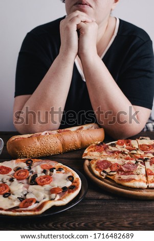 Nerve food, addiction, eating disorders, bulimia. Overweight woman sit at the table with big amount of junk food