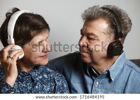 A couple listening to music together in wireless headphones. An older man and a woman enjoying music as a hobby. Staying at home during COVID-19 pandemic and enjoying hobbies. Quarantine at home.