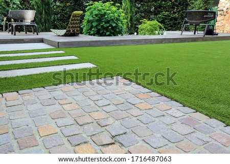 Modern garden design and terrace construction with a material mix of cobble paving stones and concrete paving slab and artificial lawn and wood Royalty-Free Stock Photo #1716487063