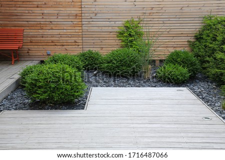 Modern garden design and terrace construction with a timber floor terrace and grass plants bush box trees in a patch with crushed stone in front of a wooden wall Royalty-Free Stock Photo #1716487066