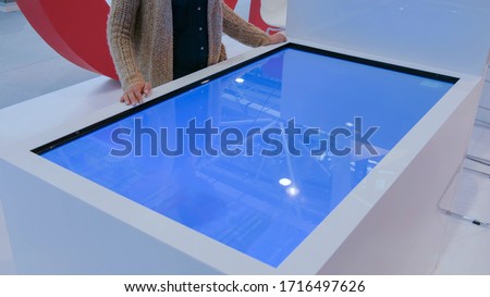 Woman using interactive touchscreen display table at urban exhibition - scrolling and touching