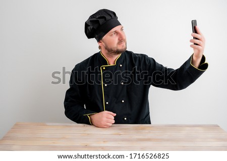 Portrait of young male chef in black uniform taking selfie photography posing on a white isolated background