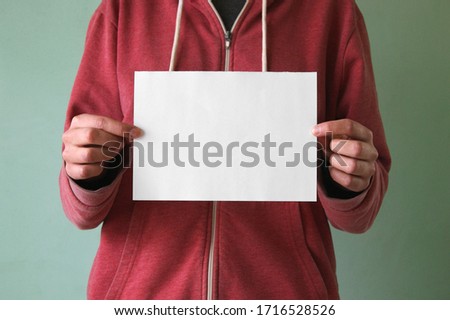 A young man holds an empty sheet of paper. Place for text.