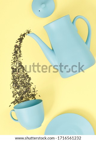 minimalism concept with light pastel colored blue teapot pouring tea and cup on yellow background.  Flat lay. Tea time concept. Empty space