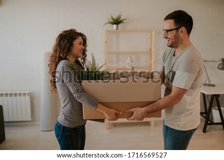 Photo of attractive young couple carrying cardboard box together. Young couple is having fun while moving in to their new home.