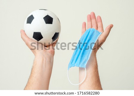 Soccer ball and medical mask in man hands up on white background.
