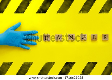 Hand in blue medical glove and  inscription on wooden cubes "Danger" on yellow background. World epidemic danger. Global pandemic. Radiation pollution.
