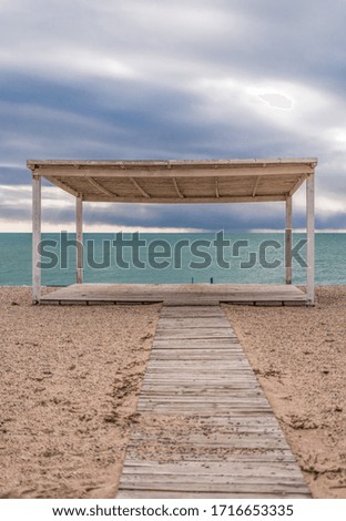 wooden walkway and sunshades on sand beach with azure sea, cloudy sky background. Empty beach with sunshades. Evpatoriya, Crimea. Copy space. The concept of calmness, silence and unity with nature.