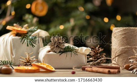 Zero waste christmas concept. Packed in natural fabric gifts and decorations from natural materials on wooden table near Christmas tree with lights