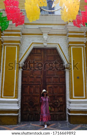 An Asian female tourist standing in front of an old decorative door of a church in Coyoacán (Place of Coyotes) neighbourhood, Mexico City, Mexico.