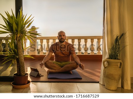 Young man is listening relaxed music with tablet and doing meditation on the patio at sunset - Healthy lifestyle, inner peace and balance concept - Quarantine balance in time of coroanvirus crisis Royalty-Free Stock Photo #1716687529