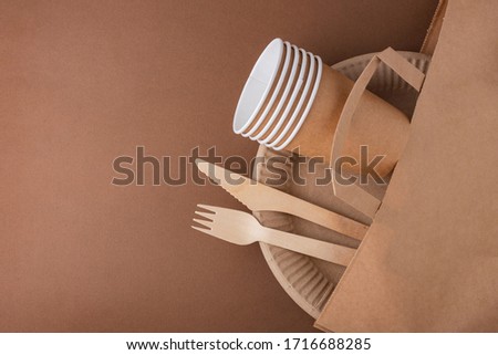 paper bag with handles, disposable eco friendly tableware, plates, glasses, Cutlery, on a brown background top view of eco waste Royalty-Free Stock Photo #1716688285