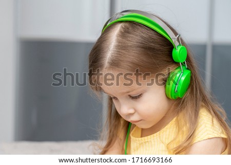 little girl with big green headphones listens to music
