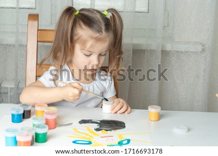 beautiful girl 3-4 years old dips a brush in a jar of white paint. children's creativity during the period of self-isolation and quarantine in connection with the coronavirus. focus on the baby's hand