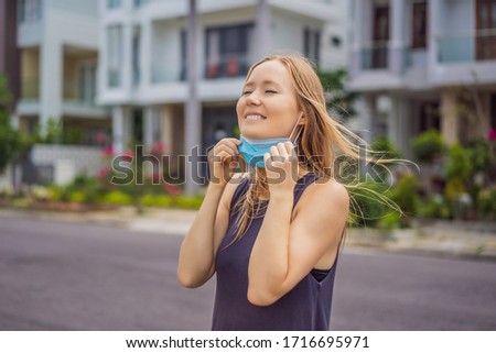 Quarantine is over concept. Woman taking off mask against the background of small town houses. We are safe. Coronavirus ended. We won. No more quarantine. Breathe deep. Take off the mask. Coronavirus Royalty-Free Stock Photo #1716695971