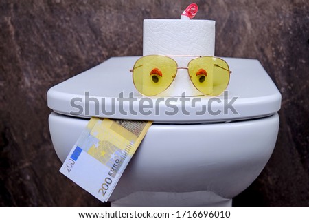 Concept of a funny toilet with eyes and tongue made of Euro bills. Humor about running out of toilet paper and spending money on it.