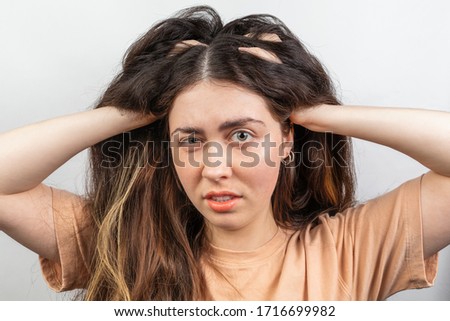 The brunette woman nervously scratches her head suffering from itching. White background. The concept of dandruff and pediculosis.